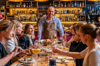 Clients joyeux partageant un moment convivial autour d'une grande table dans notre restaurant, dégustant une variété de plats savoureux et des verres de vin sous l'atmosphère chaleureuse de Serre Chevalier